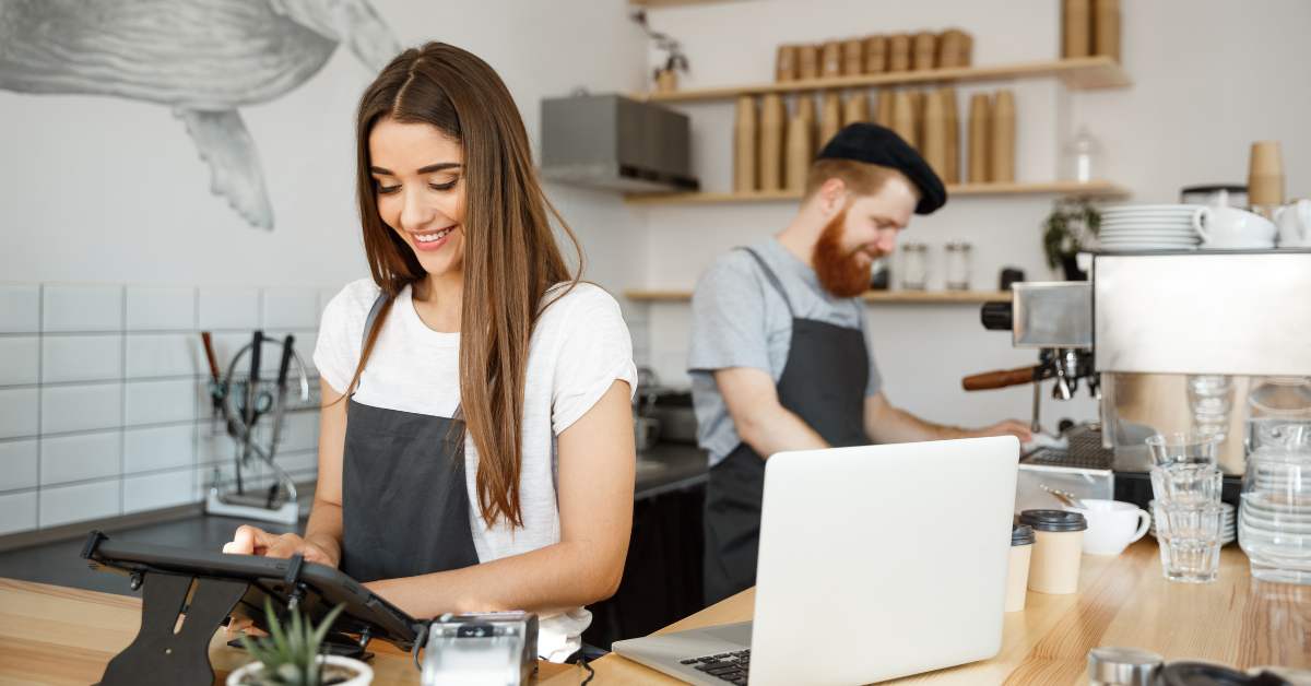 Two people working at a local coffee shop with a laptop on the counter, this image is trying to convey small business owners working on their local SEO strategy.