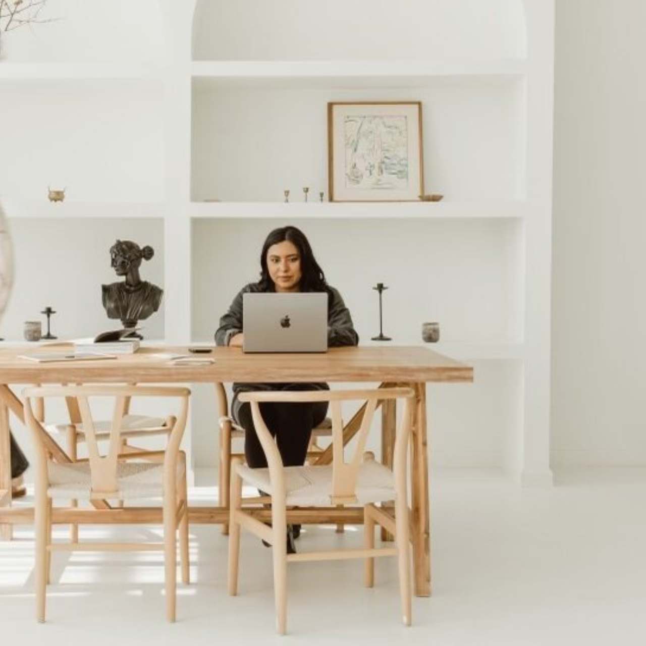 Woman named Valery, sitting at her desk, researching AI Search Visibility, sitting at a wooden rustic desk with a white aesthetic bookcase in the background.